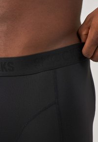 Mutande nere con una texture liscia e una comoda vita elastica con marchio. Presentano un design aderente e cuciture pulite.
