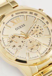 Montre en acier inoxydable doré avec un cadran texturé, des sous-cadrans chronographe et une échelle tachymétrique, dotée de marqueurs d'heure clairs et audacieux.