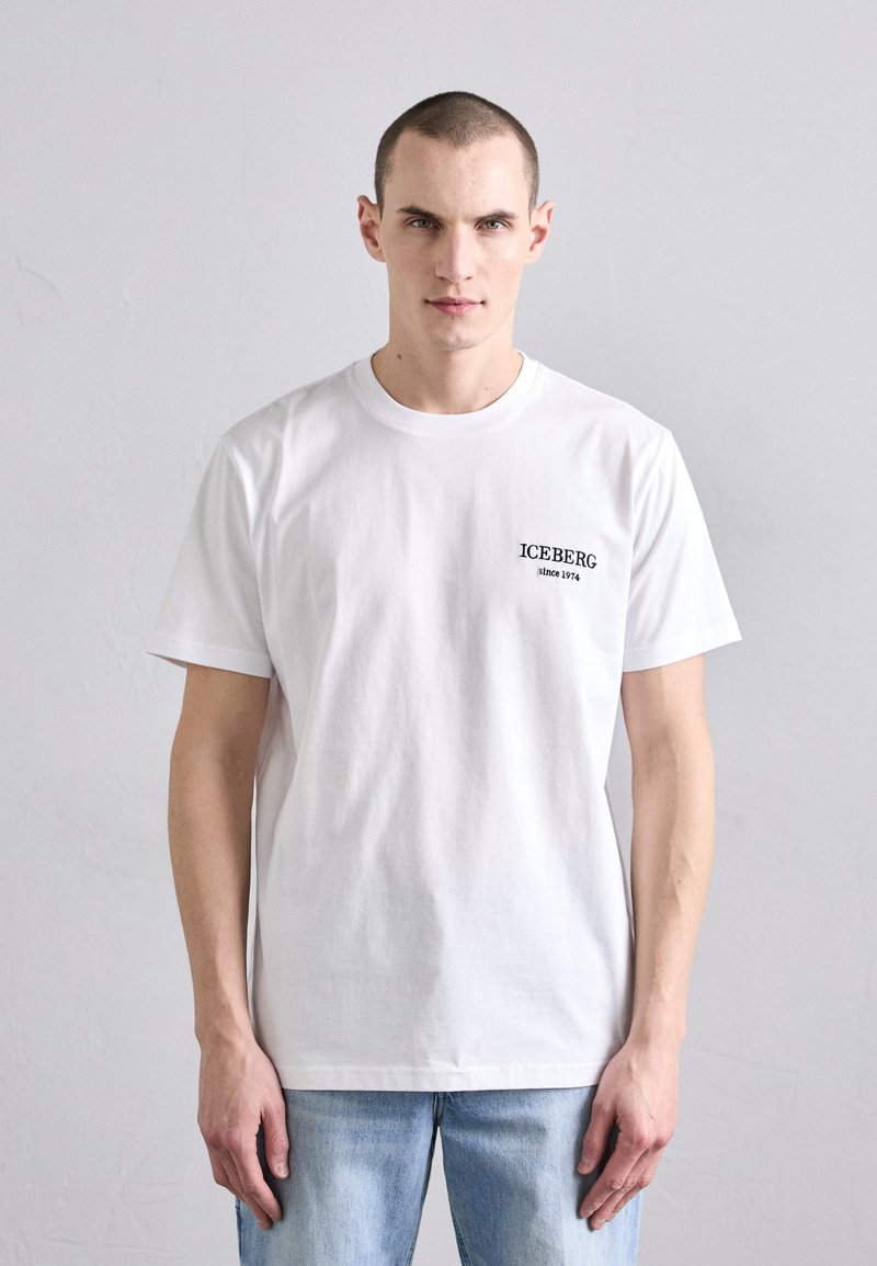 T-shirt en coton blanc à manches courtes avec un petit texte graphique noir indiquant "ICEBERG depuis 1974" sur la poitrine gauche.