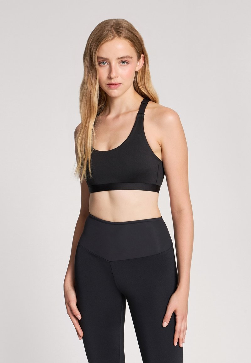 Reggiseno sportivo nero con scollatura rotonda e spalline larghe; il tessuto appare liscio ed elastico. Abbinato a leggings in vita alta dello stesso colore.