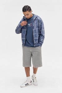 Blå mønstret zip-hoodie over en marineblå t-shirt, parret med sort-hvide ternede shorts og hvide sneakers med sorte striber. Græs-lignende tekstur.