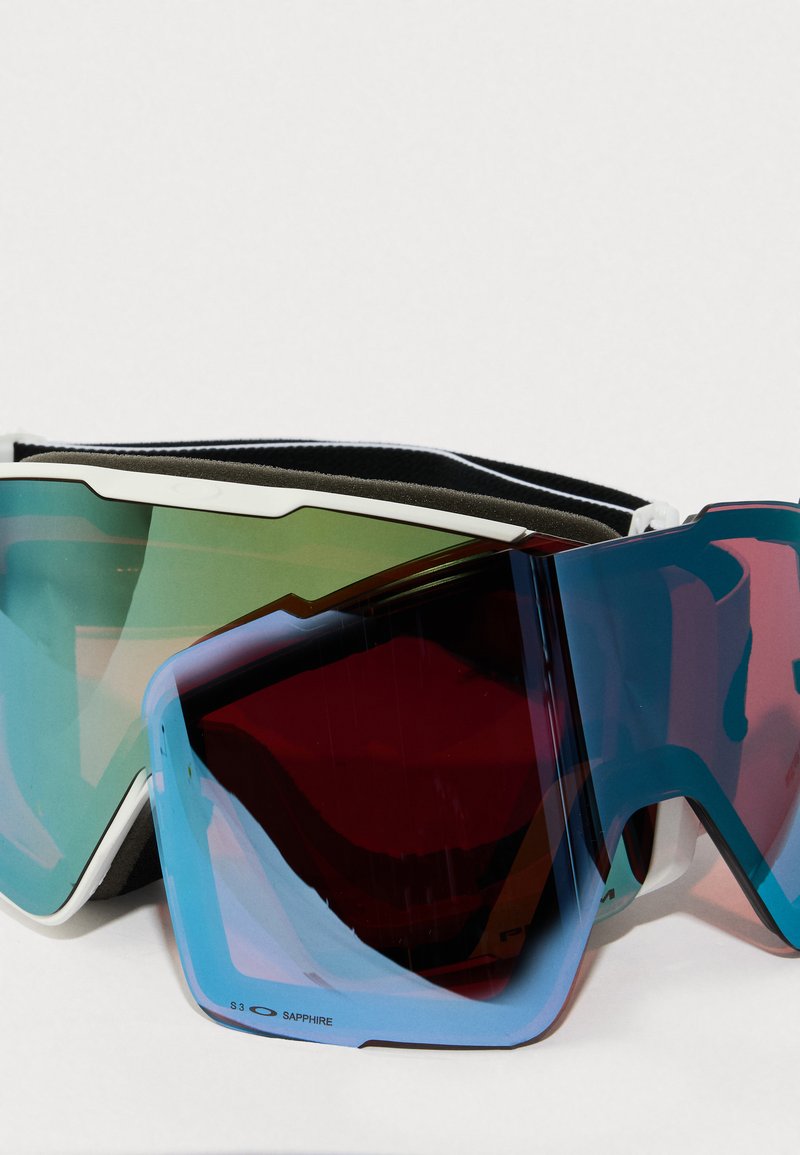 Hoge prestaties skibril met een wit en zwart frame, reflecterende groene en blauwe lenzen, en schuimrubberen padding voor comfort.