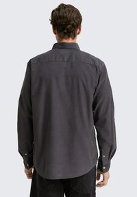 Camisa de manga larga en gris carbón con cuello abotonado y puños de un solo botón. Textura suave, con un dobladillo curvado y detalle en la parte posterior.