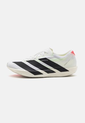 Chaussure de course blanche avec des bandes diagonales noires, des lacets et un accent rouge sur le talon, montrée de côté sur un fond uni.