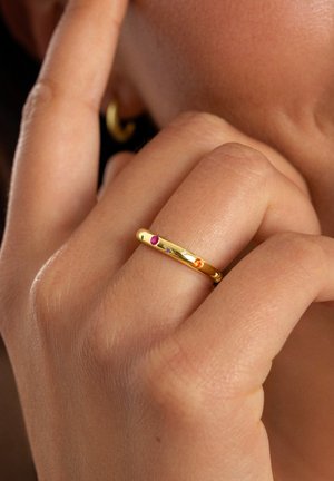 Gold ring with five small gemstones (pink, purple, orange) set along the band, smooth surface, worn on a finger against skin.
