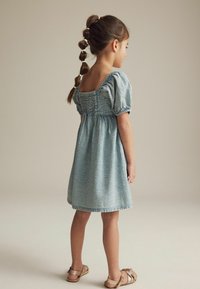 Hele sinine mustriga kleit puff-varrukatega, smockitud bodice ja laienev seelik. Kanda beežide sandaalidega; juuksed on punutud.