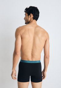 Black boxer shorts with a teal elastic waistband featuring the brand name "BJÖRN BORG." Subject shown from the back, no other details visible.