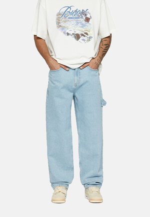 Light blue denim jeans with a straight cut, high waist, and side pockets, paired with a white graphic t-shirt and beige sneakers.