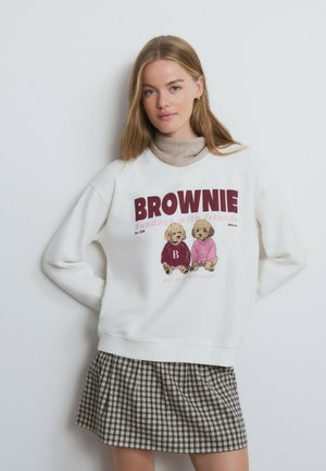 Sweatshirt blanc avec un imprimé graphique représentant deux chiots, associé à une jupe à carreaux. Tissu doux et coupe décontractée.
