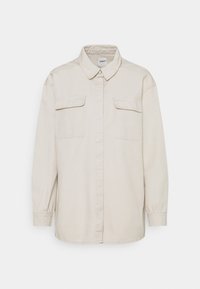 Chemise beige clair à boutons, en coton, avec manches longues, col pointu et deux poches avant. Présente une coupe décontractée et une texture lisse.