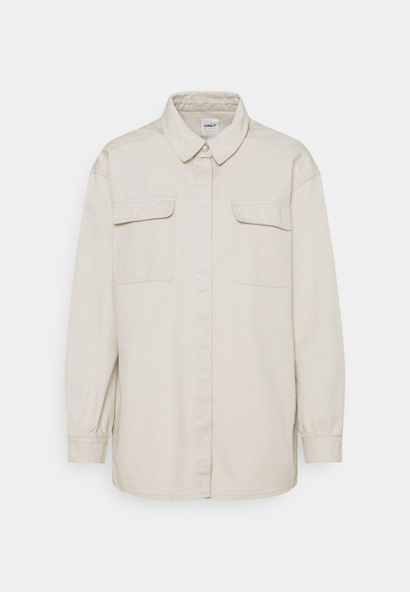 Chemise beige clair à boutons, en coton, avec manches longues, col pointu et deux poches avant. Présente une coupe décontractée et une texture lisse.