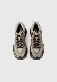 Ανοιχτό γκρι αθλητικά παπούτσια με μαύρες λεπτομέρειες. Πλέγμα επάνω μέρος, επενδεδυμένος γιακάς και μαύρα κορδόνια. Παχύ πέλμα με κίτρινη διακόσμηση, με εμφανές λογότυπο.