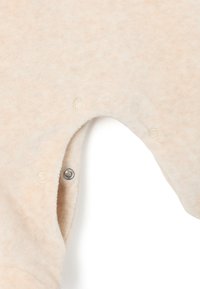 Mono de algodón beige con una textura suave, que cuenta con botones a presión y una abertura en las piernas. La tela tiene un patrón sutil para añadir detalle.