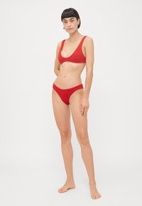 Ensemble bikini rouge avec un design minimaliste, comprenant un haut à décolleté en V profond et un bas taille basse. Tissu lisse sans motifs ou ornements visibles.