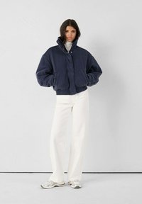 Marineblauwe fleecejas met hoge kraag en drukknopen, gecombineerd met witte wijde broekspijpen en zilveren sneakers. Eenvoudig, modern ontwerp.