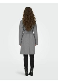 Grau-gürtelteter Mantel mit langen Ärmeln, mittellangem Design und glatter Textur. Kombiniert mit schwarzen, schmal geschnittenen Hosen und Stiefeletten.