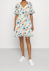 Blommig klänning med V-ringning, korta volangärmar och åtstramad midja. Har flerfärgade blommönster på en ljus bakgrund.