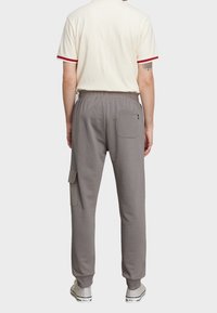 Graue Sweatpants mit einem elastischen Bund, seitlicher Cargo-Tasche und Rückentasche. Das Material wirkt weich und hat einen lockeren Sitz.