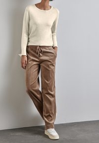 Un haut beige clair à manches longues associé à un pantalon en velours côtelé marron avec une taille élastique et un cordon de serrage. Des baskets blanches complètent la tenue.