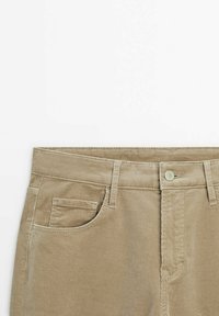 Pantalon en velours côtelé beige avec bouton à l'avant, passants pour ceinture et deux poches avant, dont une petite poche pour monnaie sur le côté droit.