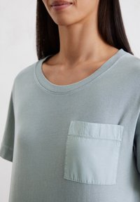 Lichtblauwe katoenen T-shirt met een ronde hals en korte mouwen, met een vierkant zakje op de linkerborst. Zachte textuur.