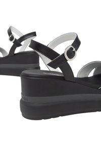 Sandali platform neri con design a incrocio e hardware circolare in argento. Suola testurizzata per una presa sicura; finitura in pelle liscia e raffinata.