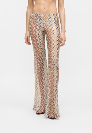 Slim-fit, high-waist trousers with a multicolored zigzag pattern, worn with open-toe black sandals.
