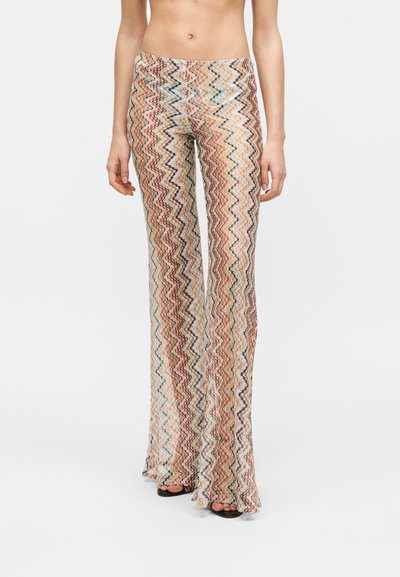 Pantalon slim taille haute avec motif zigzag multicolore, porté avec des sandales noires à bouts ouverts.