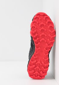 Černá atletická podrážka s výrazným červeným gumovým vzorkem s cik-cak vzorem a vyvýšenými žebry. Na podrážce je viditelný text "POC".