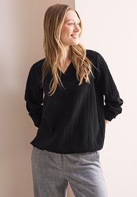 Zwarte geribbelde blouse met lange mouwen en een V-hals, met knoopdetail bij de halslijn. Gepaard met gemêleerde grijze broek.