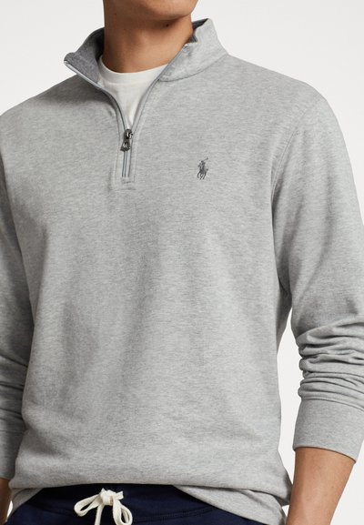 Lichtgrijze pullover van een zachte katoenmix. Beschikt over een halve rits bij de kraag en een geborduurd logo op de borst. Lange mouwen met smalle manchetten.