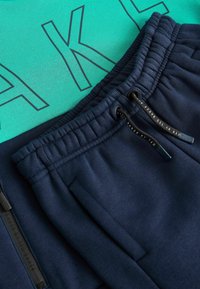 Grøn t-shirt med sort skrift placeret over navy sweatpants. Sweatpants har en elastisk talje og snorede detaljer.