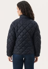 Prešívaná čierna bunda s kapucňou, s vysokým golierom, so vzorom diamantov a elastickými manžetami, skombinovaná s džínsami.