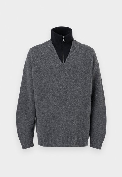 Suéter gris oscuro de cuello en V superpuesto sobre un cuello alto negro con cremallera, con puños y dobladillo acanalados, exhibido sobre un fondo blanco.