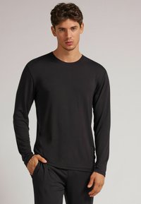 Černé tričko s dlouhým rukávem a kulatým výstřihem, vyrobené z měkkého materiálu, s uvolněným střihem a jednoduchým designem bez viditelných vzorů nebo akcentů.
