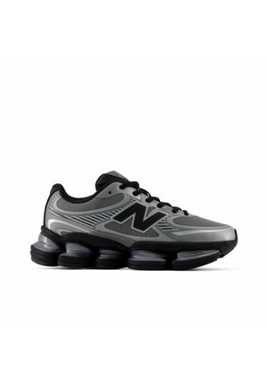 Chaussure de sport grise et noire avec dessus en mesh, grand logo "N", lacets noirs et semelle épaisse, segmentée et rembourrée.