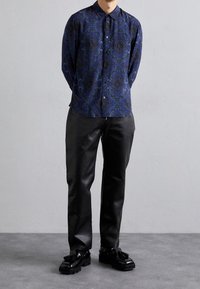 Koszula z długim rękawem w ciemnym niebieskim kolorze z misternym wzorem paisley, zestawiona z czarnymi skórzanymi spodniami i błyszczącymi czarnymi butami.