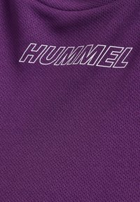 Lilla atletisk stof med et struktureret mesh-mønster. Har hvidt trykt tekst, der staver "HUMMEL." Designet er let og åndbart.