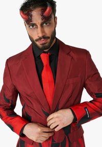 Traje rojo con patrones de llamas negras; cuenta con una corbata roja y una camisa negra. Los detalles incluyen cuernos de diablo y maquillaje oscuro en los ojos.