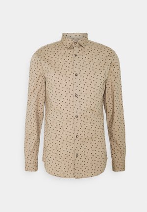 Vaalea beige nappipaita, jossa on levitetty kaulus, toistuva musta lintukuvio, pitkät hihat ja suora helma.