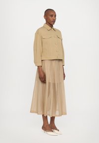 Beige cropped takki, jossa on napitus ja kaksi etutaskua, yhdistettynä virtaavaan, läpinäkyvään beigeen hameeseen ja valkoisiin teräväkärkisiin mule-korkokenkiin.