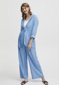 Gaiši zils, brīvi pieguļošs divdaļīgs tērps, kas sastāv no garām piedurknēm jostu nesoša žakete un platām biksēm. Izgatavots no strukturētas auduma.