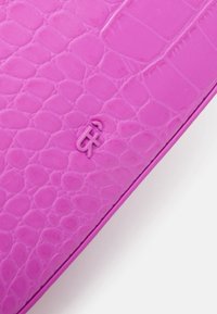 Coin de portefeuille en cuir texturé crocodile rose avec un petit symbole ampersand sur fond blanc.