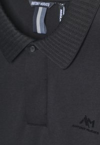 Polo shirt nera con colletto a coste testurizzato, apertura con due bottoni e un logo discreto nell'angolo inferiore. Tessuto con finitura liscia.