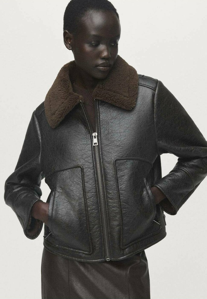Chaqueta de cuero negra con un cuello de piel sintética marrón, cierre de cremallera y bolsillos laterales. Presenta un material texturizado y un diseño corto.