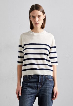Maglione lavorato a maglia color crema con strisce orizzontali blu navy, scollo rotondo e maniche corte. Abbinato a jeans in denim scuro.