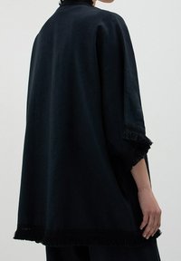 Czarna, oversize odzież z frędzlami na rękawach i u dołu, wykonana z fakturowanej tkaniny. Prosty, luźny fason dla komfortu.