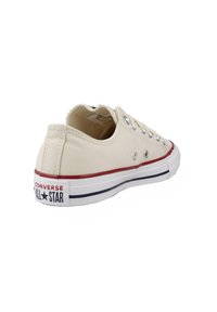 Kangaskengät vaaleanbeigellä pinnalla, joissa hopeiset metalliset silmukat, punaiset ja laivastonsiniset raidat pohjassa, ja joissa on "Converse All Star" -brändäys kantapäällä.