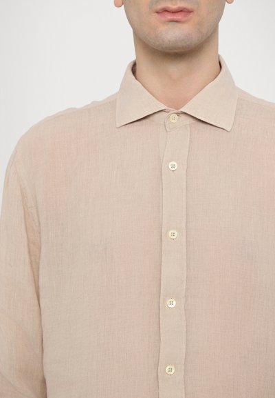 Camisa de linho bege com colarinho clássico, fecho frontal com botões claros e acabamento de tecido texturizado.