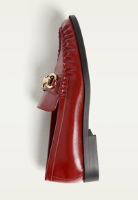 Red leather loafer with a glossy finish, featuring a gold-tone hardware accent and stitched detailing along the upper. Flat black sole.
